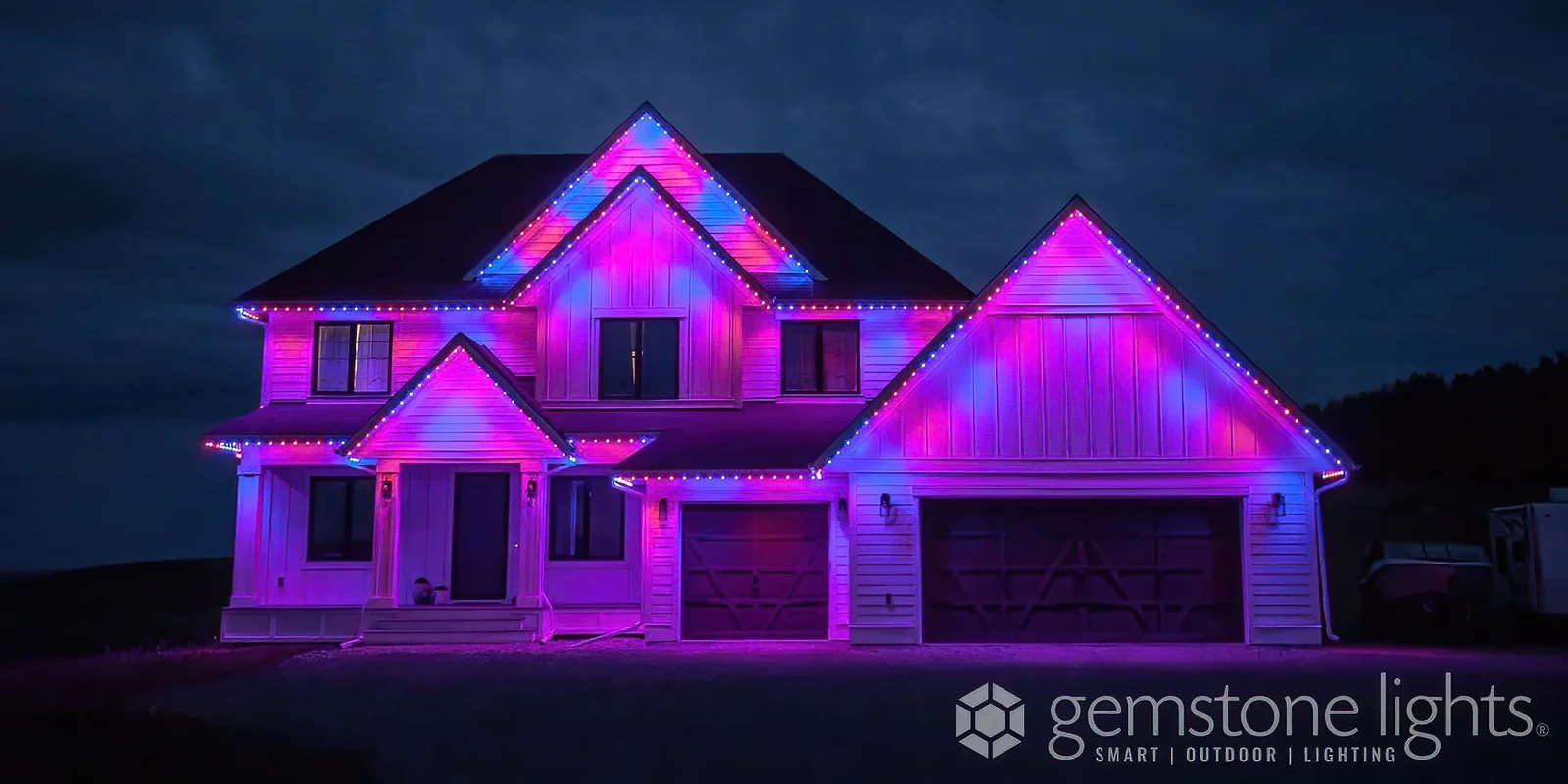 A house is illuminated with vibrant pink and blue lighting against a dark sky