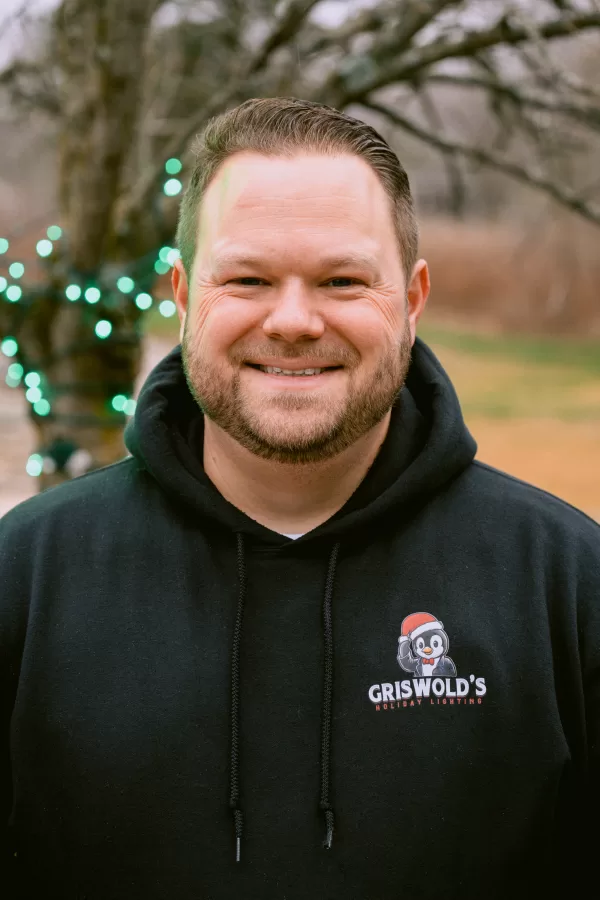 A smiling man wears a black hoodie in a scenic outdoor setting
