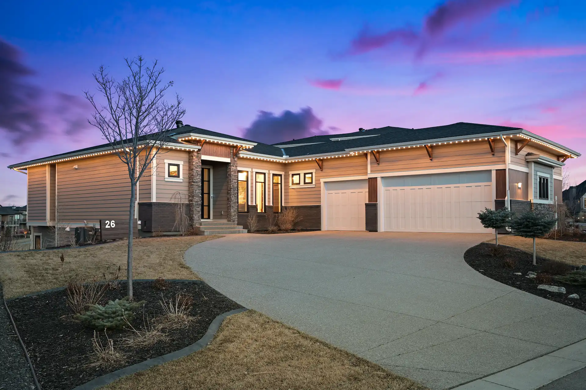 A modern house with a spacious driveway is illuminated at dusk