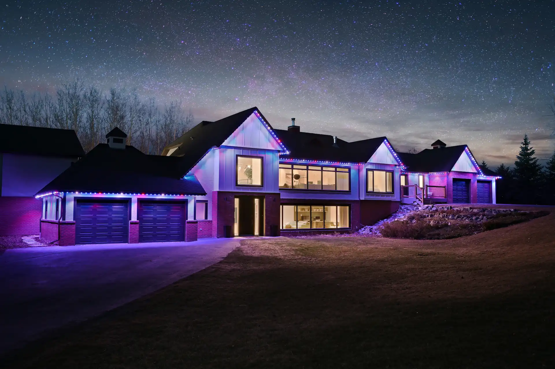 A modern house is beautifully illuminated with colorful lights under a starry night sky