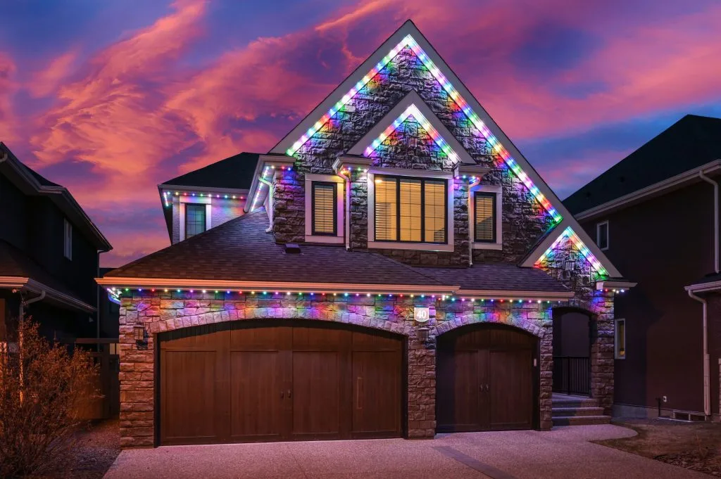 A beautifully decorated house with colorful lights twinkles under a vibrant sunset sky