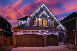 A beautifully decorated house with colorful lights twinkles under a vibrant sunset sky